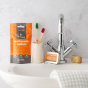 Ecoliving orange flavour toothpaste tablets tin leaning against a silver tap, next to a white toothpaste holder and a bag of Ecoliving orange toothpaste tablets