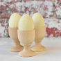 Three of the Erzi Six White Eggs Wooden Play Food in wooden egg cups with brick wall background