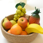 A natural woven basket holding a selection of Erzi wooden toy fruits.
