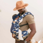 Tula - A man carries a child on his chest wearing a Coast Whale Watch - Explore Baby Carrier. This is a side-on lifestyle shot with a soft cream background. The baby is facing the man's chest in the carrier.