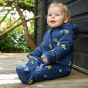 A child sits outdoors wearing the Frugi Waterproof All-In-One Suit - Buzzy Bee.