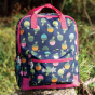 Frugi Explorers Backpack - Acorns / Honeysuckle. The bag sits on a rock in an outdoor setting.