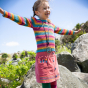 A child wears the Frugi Zoe Knitted Jumper - Rosehip Rainbow Stripe in an outdoor setting.