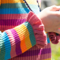 A child wears the Frugi Zoe Knitted Jumper - Rosehip Rainbow Stripe in an outdoor setting, this is the Cuff detail on the jumper.