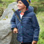 A young child stands outdoors wearing the Frugi Rambler 3 in 1 Coat - Indigo.
