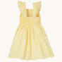 The back of the the Frugi Jasmine Dress - Flowers made from GOTS Organic cotton. A light sunshine, yellow and white striped short sleeve dress with adjustable ruffle straps, smocked back, and a gathered waist band, on a cream background. 