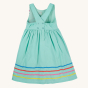 The back of the Frugi Organic Phebe Party Dress - Spring Mint / Macaw, showing the shoulder straps, button fastenings, elasticated back and colourful piping going around the whole skirt section of the dress. On a cream background