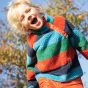A child wears the Frugi Coral Reversible Snuggle Fleece - Paprika Rainbow Stripe / Indigo in an outdoor setting.