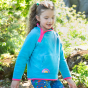 A child wears the Tor Blue option of the Frugi Coral Reversible Snuggle Fleece - Honeysuckle Stripe / Tor Blue in an outdoor setting.