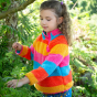 A child wears the Honeysuckle Stripe option of the Frugi Coral Reversible Snuggle Fleece - Honeysuckle Stripe / Tor Blue in an outdoor setting.