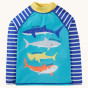 The front of the Frugi Rash Vest Sun Safe - Shark.  A blue sun-safe rash vest with a yellow neck, blue and white striped arms and fun shark print on the front, on a cream background. This rash vest passes British Sun-safe standards UPF 40+ and is made wit