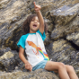A child sat on a large rock and pointing into the distance, wearing the Frugi Children's Organic Cotton Robbie Raglan T-Shirt - Squid. A soft 100% organic cotton t-shirt with a white body, contrasting blue raglan sleeves, and features a playful squid shoo