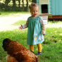 A young girl is outside a chicken coup wearing the Frugi Agatha Cord Dress - Chicken.