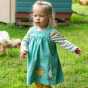 A young girl strides through chickens grazing wearing the Frugi Agatha Cord Dress - Chicken.