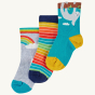 Frugi Children's Organic Cotton Little Socks 3 Pack - Sloths. The sock at the front is blue with an adorable sloth hanging from the cuff and yellow heels and toes, the sock at the back features a rainbow on grey, and the sock int eh middle is a bright str