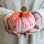 Glosters Handmade Medium-sized Autumn Ceramic Pumpkin -  Orange Drip Glaze. A person holds the pumpkin in the palms of their hands to show its scale.