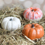 Glosters Handmade Medium-sized Autumn Ceramic Pumpkin - Speckled Orange. The ceramic pumpkin sits on a wooden surface surrounded by straw and other coloured pumpkins.