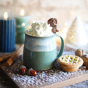 Glosters Pottery Sage Green Mug. A handmade stoneware mug by Glosters Pottery in Sage is a grey-green mug with fluid drippy white glaze, which looks like sea foam crashing against the beach. The mug is filled with a hot drink, whipped cream and a chocolat