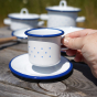 an adults hand holding the cup from the Glückskäfer Enamel Cup and Saucer set