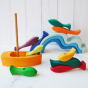 A wooden stacker set of various shapes, colours, and sizes of fish. The set includes a wooden boat with a sail on which the fish shapes are stacked. In the background, we see Grimm's wooden wave set.