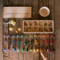 The Grapat Mis & Match play set, includes a wooden storage board with colourful dots, and small colourful cubes in various colors all line up in a row. The lid of the box has small painted dots in various colours and is on a wooden background. The photo a