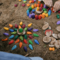 A creative mandala display on a sandy beach using the Grapat Rainbow Snowflake mandala pieces, and small wooden disks