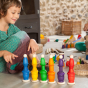 Grapat Nin Mates & Coins Wooden Toy Set. A rainbow coloured set of wooden Nin peg dolls and their corresponding Mates (cups) and coins, for open ended Waldorf and Montessori play. Child playing with multiple Grapat sets, stacking and colour matching at ho