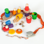 Grapat Nin Mates & Coins Wooden Toy Set. A rainbow coloured set of wooden Nin peg dolls and their corresponding Mates (cups) and coins, for open ended Waldorf and Montessori play. In a play scene with other natural loose parts. White background. 