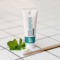 Green People Fresh Mint & Aloe Vera Toothpaste with Fluoride pictured next to a bamboo toothbrush next to a sprig of fresh mint on a tiled surface