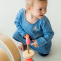 Grimm's Small Conical Stacking Tower - Neon Pink - On a plain blue background. A child looks off camera right whilst playing with the toy. Grimm's Neon Pink Friends are also in the scene.