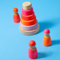 Grimm's Small Conical Stacking Tower - Neon Pink - On a plain blue background. Grimm's Neon Pink Friends are in front and behind the Tower. 