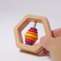 Grimm's Wooden Hexagon Baby Rattle in an adults hand on a grey background