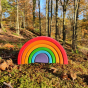 Grimm's Wooden Medium Rainbow outside with a woodland background