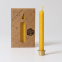 A pack of 12 Grimm's amber 100% beeswax candles in a cardboard box with one candles at the front in a brass holder. White background.