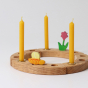Three Grimm's amber 100% beeswax candles in a celebration ring with flower and bee decorative figures. White background.