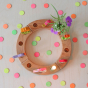 Grimm's Neon Celebration Confetti Dots. The dots surround a celebration ring on a wooden table.
