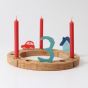 Three Red 10% beeswax candles by Grimm's in a brass holder and house, car and number three decorative figures in a celebration ring. White background
