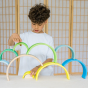 Grimm's 10-Piece Rainbow - Neon Green. A child plays in his house, creating a bridge construction from individual rainbow pieces.