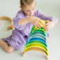 Grimm's 10-Piece Rainbow - Neon Green. A child plays in her house constructing a tower with individual rainbow puzzle pieces.