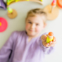 Child holding one of the Grimm's 3 Friends Wooden Peg People Neon Mix surrounded by wooden toys from the NEON range out of focus in the background.