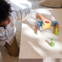 A child happily playing with the Grimms Wooden Pastel Duo Blocks. The child is in the process of building with a Grimms friend watching on