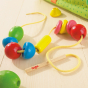 The HABA Bambini Beads on a wooden floor, showing the colourful beads threaded on a yellow cord