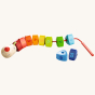 HABA Number Dragon Threading Game is made up of 10 rainbow coloured triangular wooden beads numbered 1 to 10 and a cheerful dragon's head with a cord and wooden threading needle. This image shows the triangular number beads on and off the red cord to show