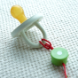 A close up of how a Heimess Baby Teether Chain attaches pictured attached to a pacifier. A Hevea bumibebe pacifier is used in the photo