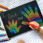 Close up of some child drawing some rainbow coloured hands on a Hellion Toys eco-friendly chalking board on a white blanket