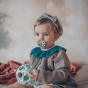 A child with a blue bow, blue eyes and a blue pacifier holds the blue Hevea Natural Rubber Upcycled Star Activity Ball 