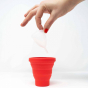Hey Girls red Menstrual Cup Sterilising Pot with a small white menstrual cup being placed inside on a white background