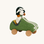 Side view of Olli Ella Holdie Dog-go Racer Boy in a green felt racing car with wooden wheels and white stripes, and a green and white felt racing hat on a cream background