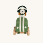 Front view of Olli Ella Holdie Dog-go Racer Boy in a green felt racing car with wooden wheels and white stripes, and a green and white felt racing hat on a cream background