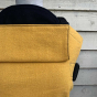 Close up of an ochre organic linen Integra baby carrier in front of a wooden fence 
